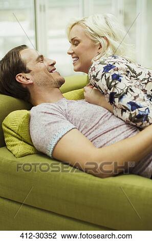 Stock Image - Affectionate couple laying on living room sofa face to face. Fotosearch
