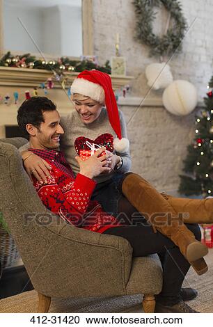 Stock Image - Affectionate couple opening Christmas gifts in living room. Fotosearch