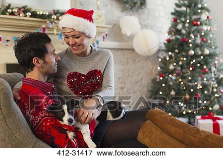 Affectionate couple with dog relaxing in living room with Christmas tree View Large Photo Image Stock Photo - Affectionate couple with dog relaxing in living room with Christmas tree. Fotosearch