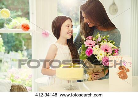 Stock Photo - Affectionate daughter giving flower bouquet to mother on Mothers Day. Fotosearch