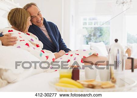 Affectionate mature couple in bathrobes enjoying breakfast in bed View Large Photo Image Stock Photo - Affectionate mature couple in bathrobes enjoying breakfast in bed. Fotosearch