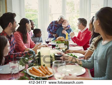 Stock Photo - Affectionate multi-ethnic senior couple hugging at family Christmas dinner table. Fotosearch