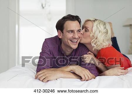 Stock Photograph - Affectionate wife kissing smiling husband on bed. Fotosearch