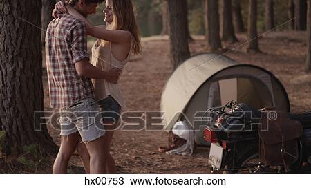 Stock Image - Affectionate young couple hugging outside tent in woods. Fotosearch