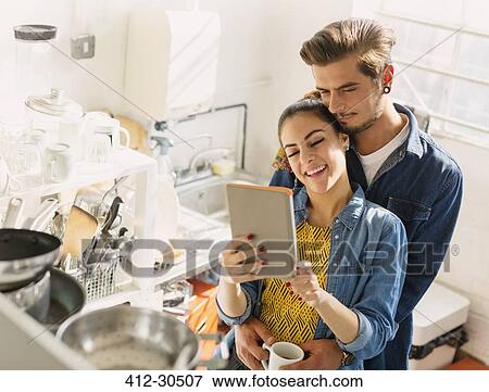 Stock Photo - Affectionate young couple using digital tablet in apartment kitchen. Fotosearch