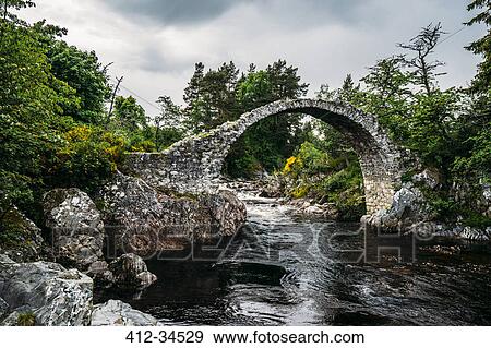 Stock Photo - Arched footbridge over tranquil stream, Carrbridge, Scotland. Fotosearch