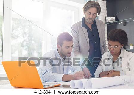Stock Image - Architects discussing blueprints in office meeting. Fotosearch