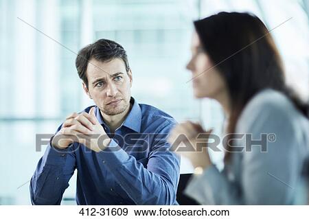 Stock Photo - Attentive serious businessman listening to businesswoman in meeting. Fotosearch