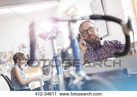Bicycle leaning against desk next to male design professional talking on cell phone in office View Large Photo Image Stock Image - Bicycle leaning against desk next to male design professional talking on cell phone in office. Fotosearch