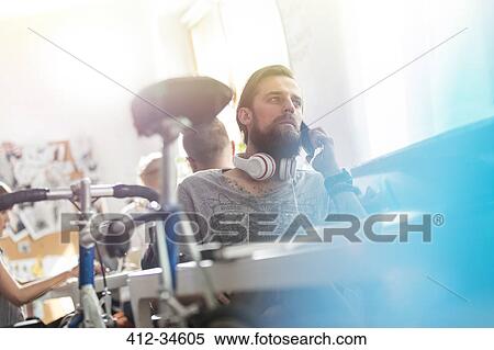 Stock Photography - Bicycle leaning against desk next to serious male design professional with headphones talking on cell phone. Fotosearch