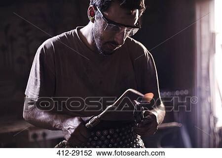 Stock Image - Blacksmith heating metal with blowtorch in forge. Fotosearch
