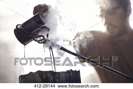 Blacksmith pouring steaming liquid over wrought iron View Large Photo Image Picture - Blacksmith pouring steaming liquid over wrought iron. Fotosearch