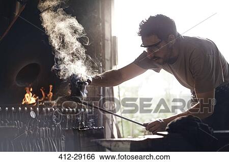 Stock Photograph - Blacksmith shaping steaming wrought iron in forge. Fotosearch