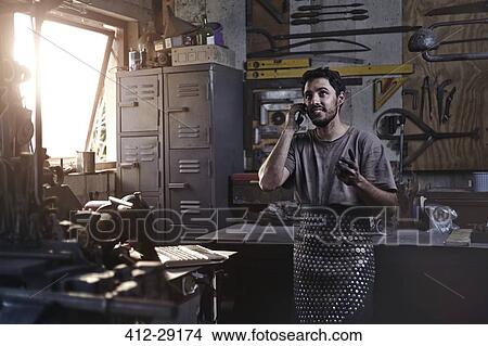 Blacksmith talking on cell phone in forge View Large Photo Image Picture - Blacksmith talking on cell phone in forge. Fotosearch