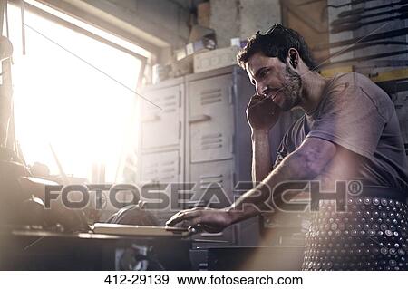 Stock Photo - Blacksmith talking on cell phone in forge. Fotosearch