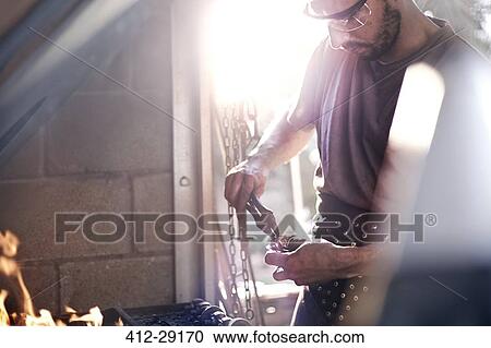 Stock Image - Blacksmith using pliers at fire in forge. Fotosearch