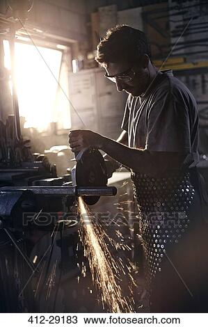 Stock Image - Blacksmith using saw in forge. Fotosearch
