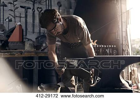 Stock Image - Blacksmith working at anvil in forge. Fotosearch
