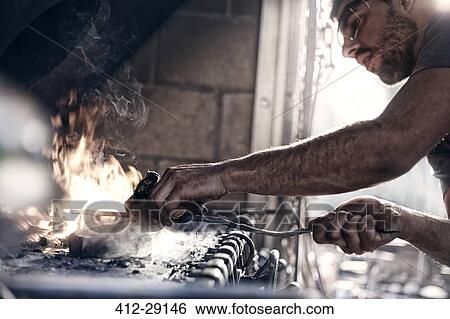 Stock Photograph - Blacksmith working over fire in forge. Fotosearch