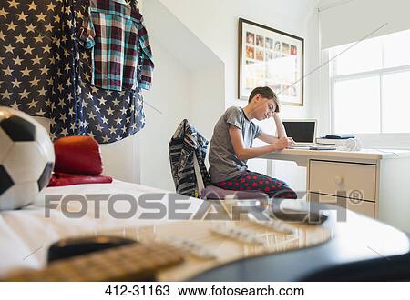 Stock Image - Bored boy doing homework at desk in bedroom. Fotosearch