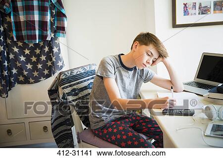 Stock Image - Bored boy doing math homework at desk in bedroom. Fotosearch