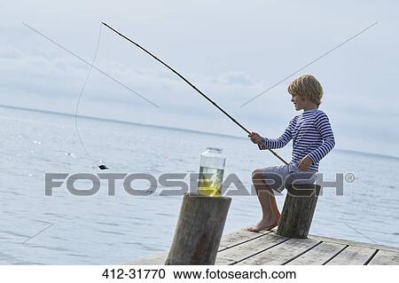 Stock Image - Boy fishing off lakeside dock. Fotosearch