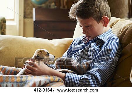 Boy holding puppy in lap on sofa View Large Photo Image Stock Photo - Boy holding puppy in lap on sofa. Fotosearch