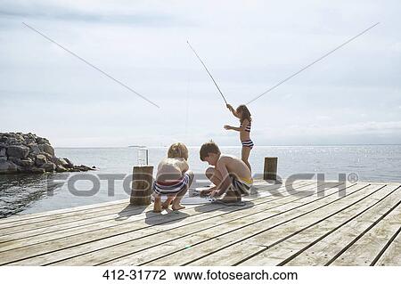 Stock Image - Boys and girl fishing off sunny lakeside dock. Fotosearch