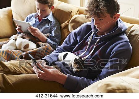 Boys using digital tablet and cell phone with puppies sleeping in laps View Large Photo Image Picture - Boys using digital tablet and cell phone with puppies sleeping in laps. Fotosearch