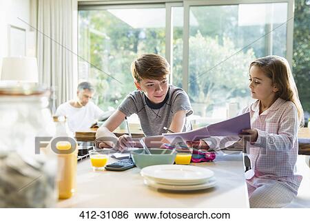 Stock Photograph - Brother and sister eating breakfast and doing homework. Fotosearch