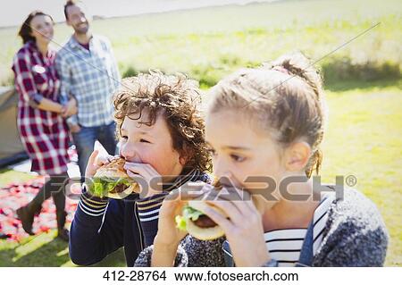 Brother and sister eating hamburgers at sunny campsite View Large Photo Image Picture - Brother and sister eating hamburgers at sunny campsite. Fotosearch
