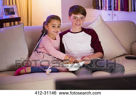 Brother and sister eating popcorn and watching TV in living room View Large Photo Image Stock Photograph - Brother and sister eating popcorn and watching TV in living room. Fotosearch
