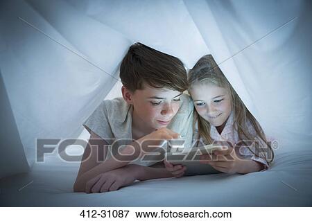 Brother and sister sharing digital tablet under sheet View Large Photo Image Stock Photo - Brother and sister sharing digital tablet under sheet. Fotosearch