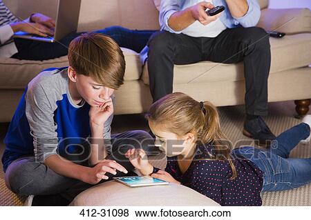 Brother and sister sharing digital tablet in living room View Large Photo Image Stock Photo - Brother and sister sharing digital tablet in living room. Fotosearch