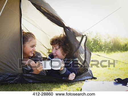 Stock Image - Brother and sister toasting mugs in tent. Fotosearch