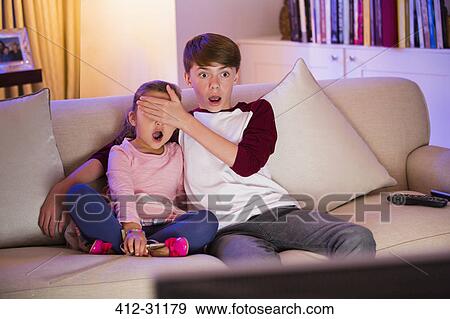 Brother covering surprised sisters eyes watching TV in living room View Large Photo Image Stock Photo - Brother covering surprised sisters eyes watching TV in living room. Fotosearch