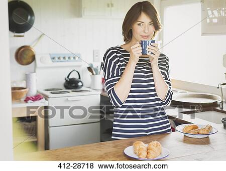 Stock Photo - Brunette woman drinking coffee in kitchen. Fotosearch