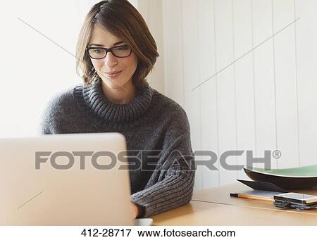 Brunette woman in sweater using laptop at table View Large Photo Image Stock Photo - Brunette woman in sweater using laptop at table. Fotosearch
