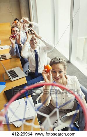 Business people aiming plastic balls at basketball hoop in conference room View Large Photo Image Picture - Business people aiming plastic balls at basketball hoop in conference room. Fotosearch