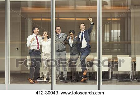 Stock Image - Business people celebrating and cheering at conference room window. Fotosearch
