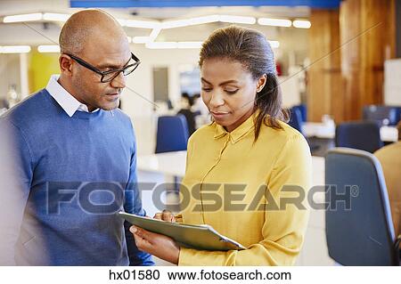 Stock Image - Business people discussing paperwork in office. Fotosearch
