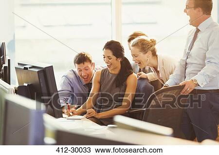 Stock Image - Business people laughing at desk in office. Fotosearch
