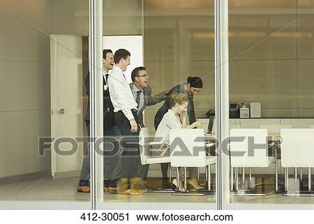 Stock Image - Business people laughing at laptop in conference room. Fotosearch