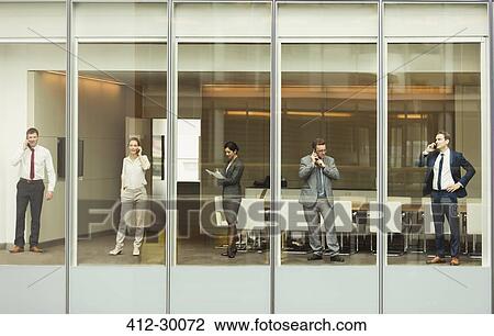 Business people talking on cell phones and reviewing paperwork at conference room window View Large Photo Image Stock Image - Business people talking on cell phones and reviewing paperwork at conference room window. Fotosearch