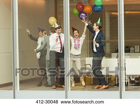 Business people wearing party hats and dancing with balloons at conference room window View Large Photo Image Stock Photo - Business people wearing party hats and dancing with balloons at conference room window. Fotosearch