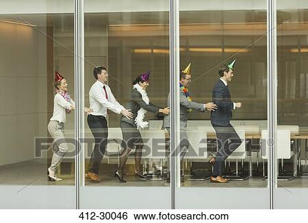 Stock Photograph - Business people wearing party hats dancing in conga line at conference room window. Fotosearch