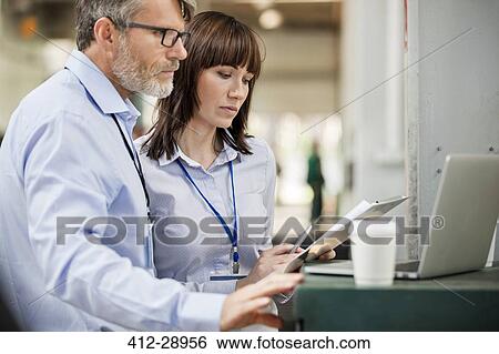 Business people with clipboard working at laptop in factory View Large Photo Image Stock Photograph - Business people with clipboard working at laptop in factory. Fotosearch