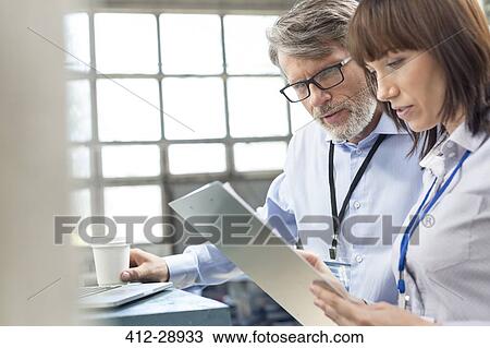 Business people with coffee reviewing clipboard in factory View Large Photo Image Stock Image - Business people with coffee reviewing clipboard in factory. Fotosearch