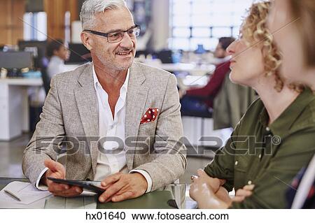 Stock Image - Business people with digital tablet talking in meeting. Fotosearch