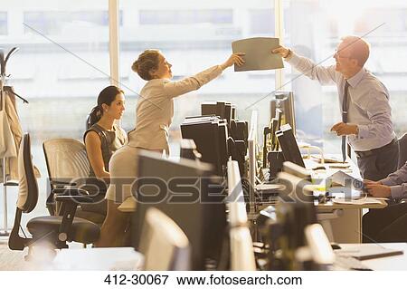 Stock Photo - Businessman and businesswoman passing folder over computers in office. Fotosearch